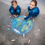 Two smiling girls drawing Earth with chalks on street