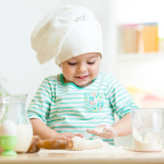 smiling baker kid girl in chef hat at kitchen