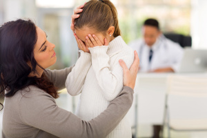 loving mother comforting her sick daughter in doctor's office