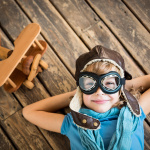 Child pilot with vintage plane toy on grunge wooden background