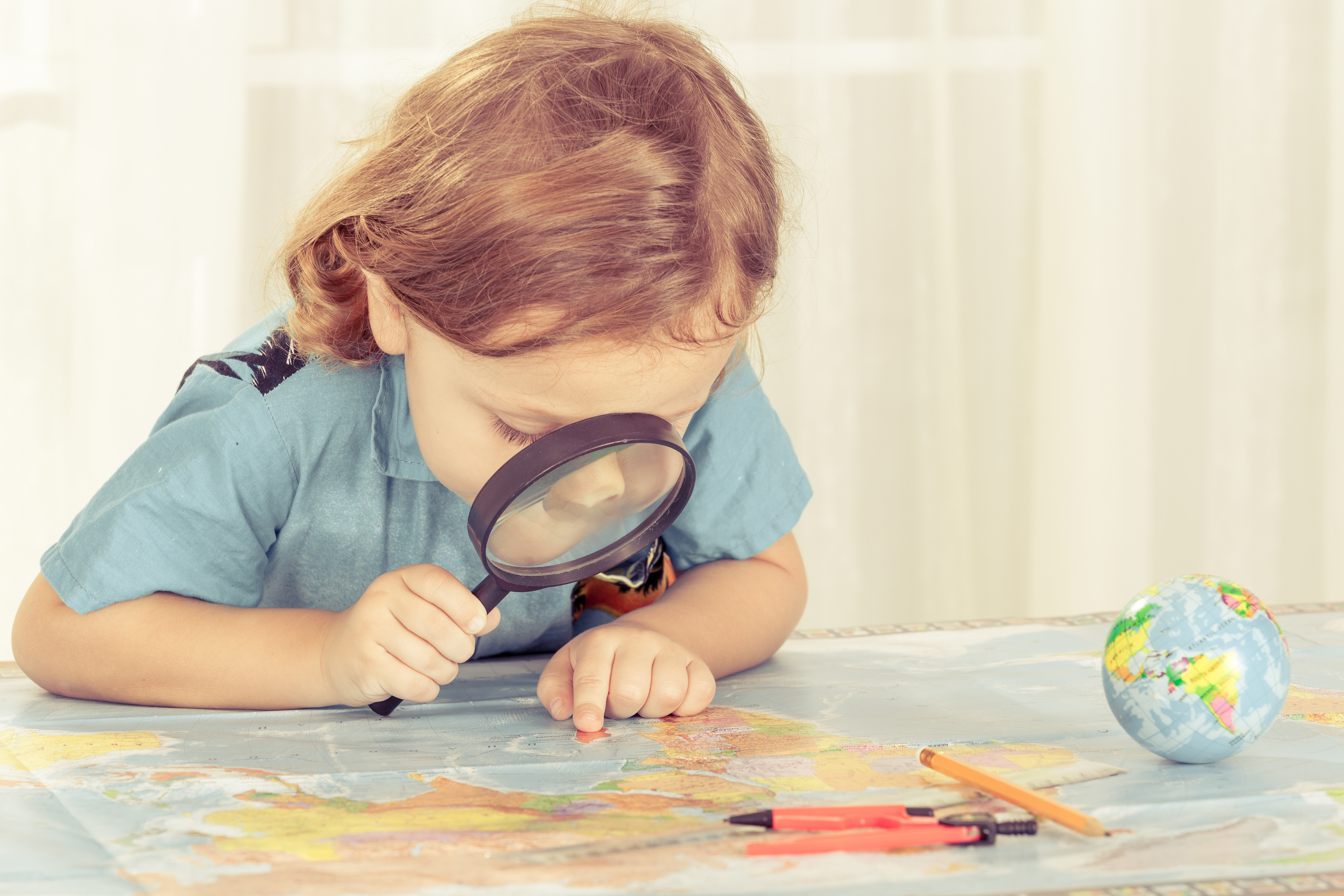 little boy considering a world map with a magnifying glass